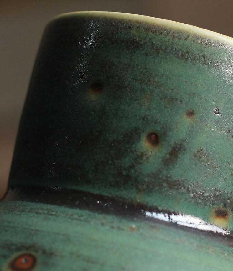 Close-up of a small sage green ceramic vase with rustic speckled glaze.